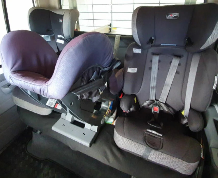 Two child car seats inside a vehicle, one purple and one gray.