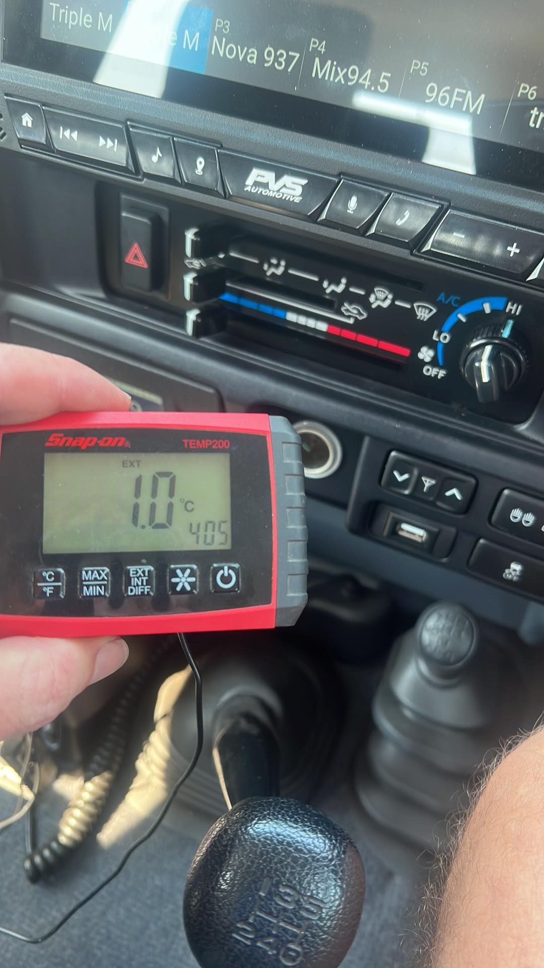 Digital thermometer held in front of a car dashboard with temperature display