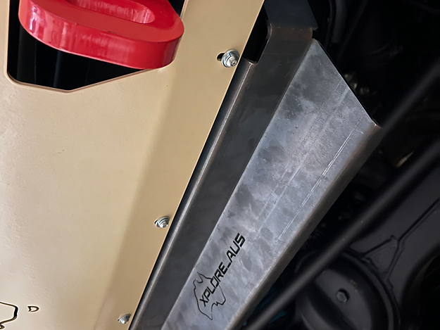 Close-up of a vehicle's Radiator Protector with 'xploreaus' branding on a beige and black background.
