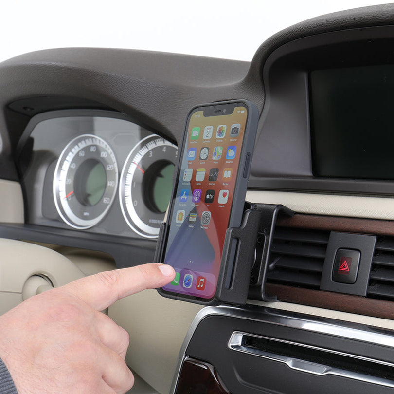 Hand using a smartphone in a car mount on a vehicle's dashboard.