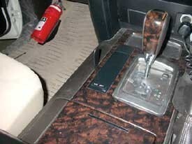 Car interior with gear shift and foot pedals on a brown floor mat.