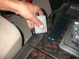Hand holding a ClicOn Dash Mount above a car's dashboard with a phone and wallet on the console.