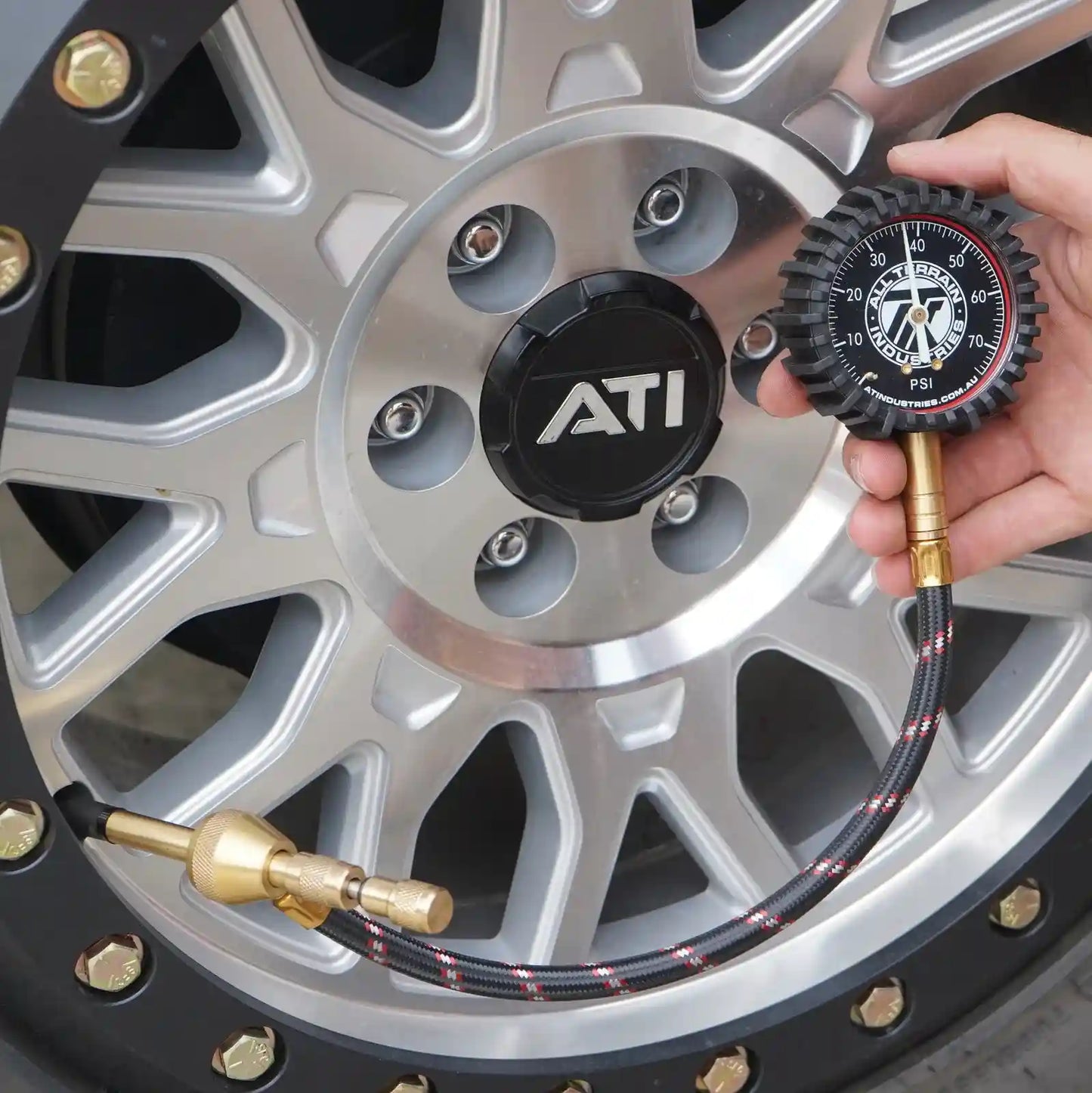 Person checking tire pressure with an ATI brand tire pressure gauge on a car wheel.