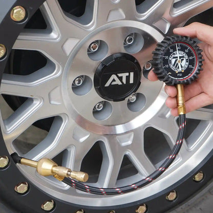 Person checking tire pressure with an ATI brand tire pressure gauge on a car wheel.