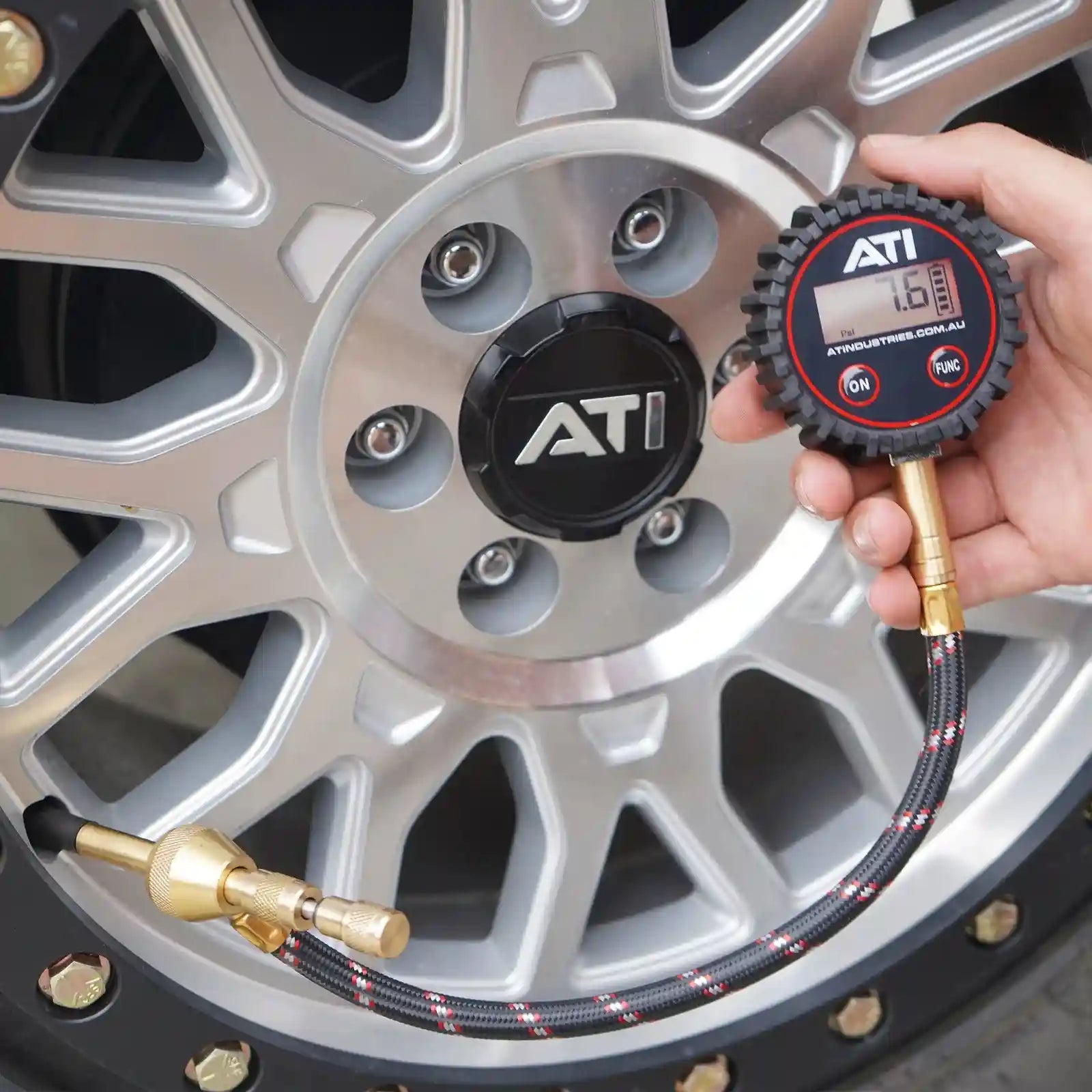 Hand using a digital tire pressure gauge to check the pressure of a car tire, with the ATI logo visible.