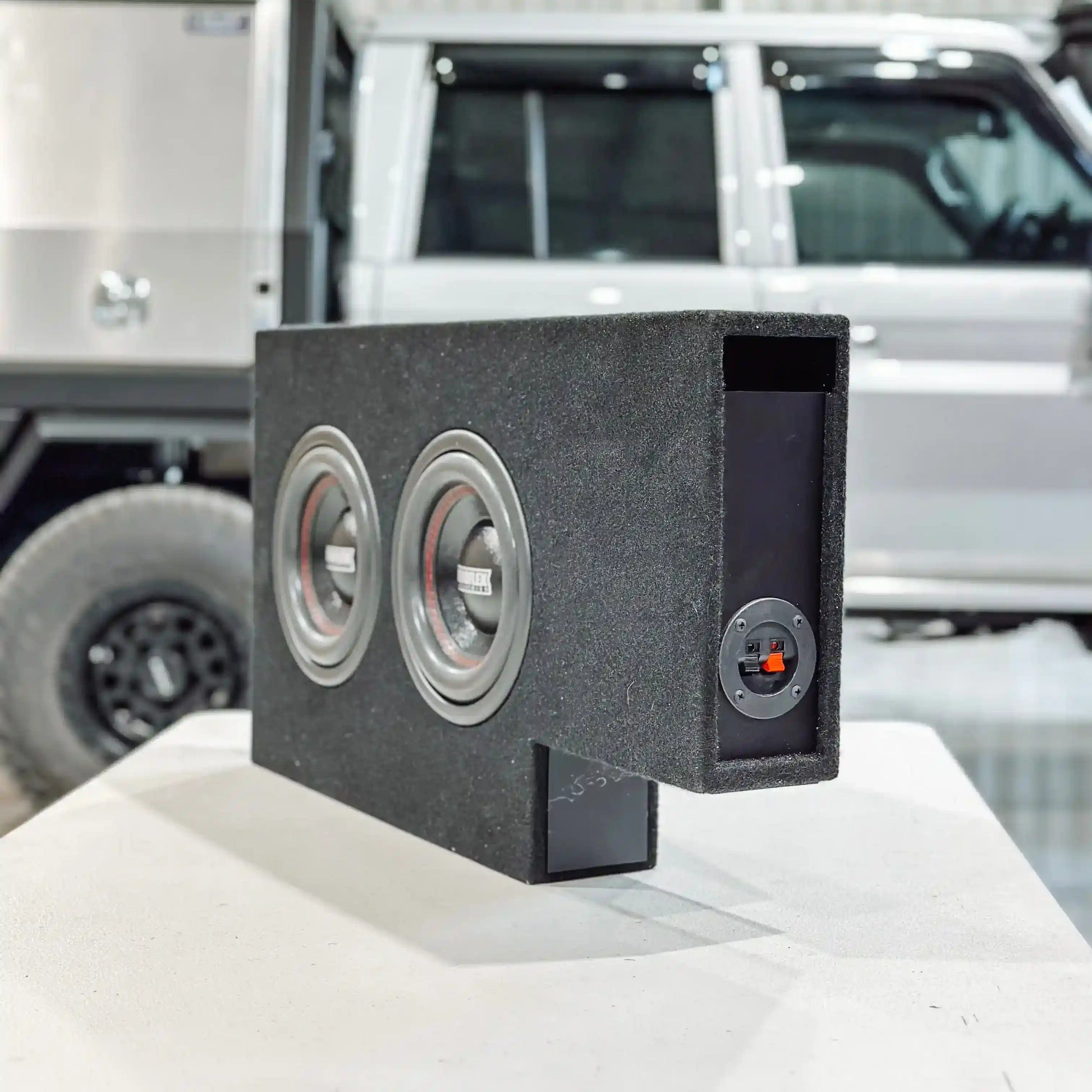 Car subwoofer box on a car's open trunk with a white SUV in the background