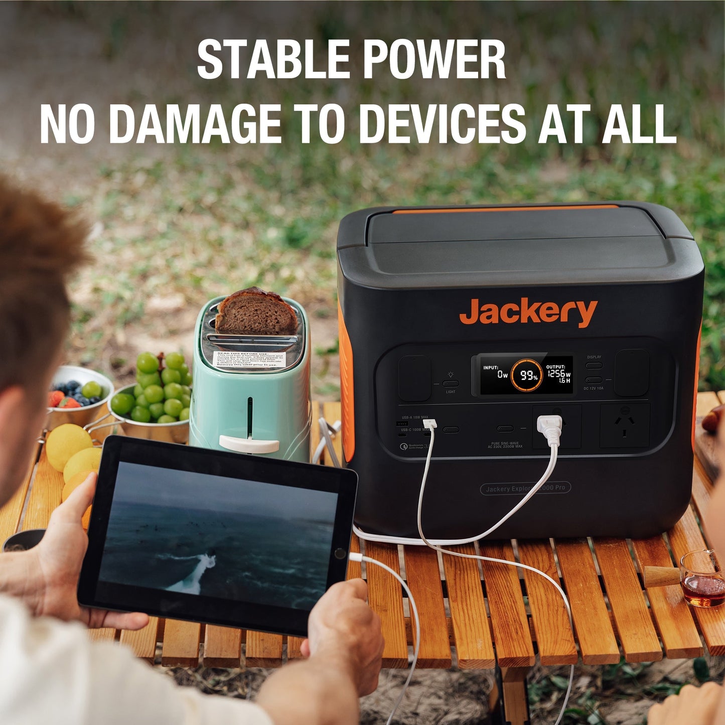 Jackery power station with a tablet, toaster, and snacks on a table outdoors.