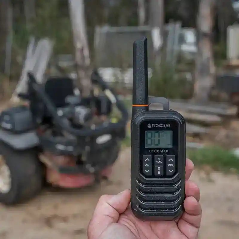 Hand holding a black walkie-talkie with a blurred background of outdoor equipment.