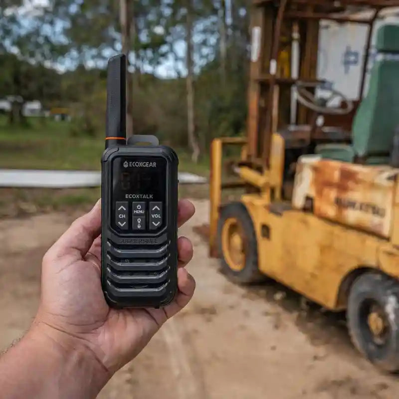 Person holding a walkie-talkie with a forklift in the background