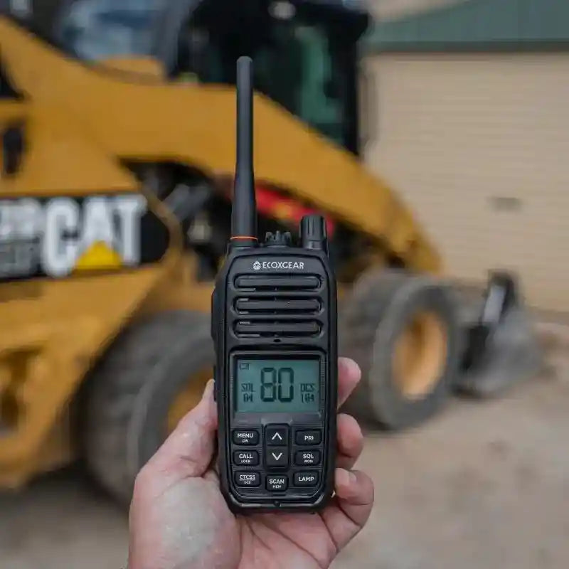 Hand holding UHF Radio with a blurred Caterpillar tractor in the background