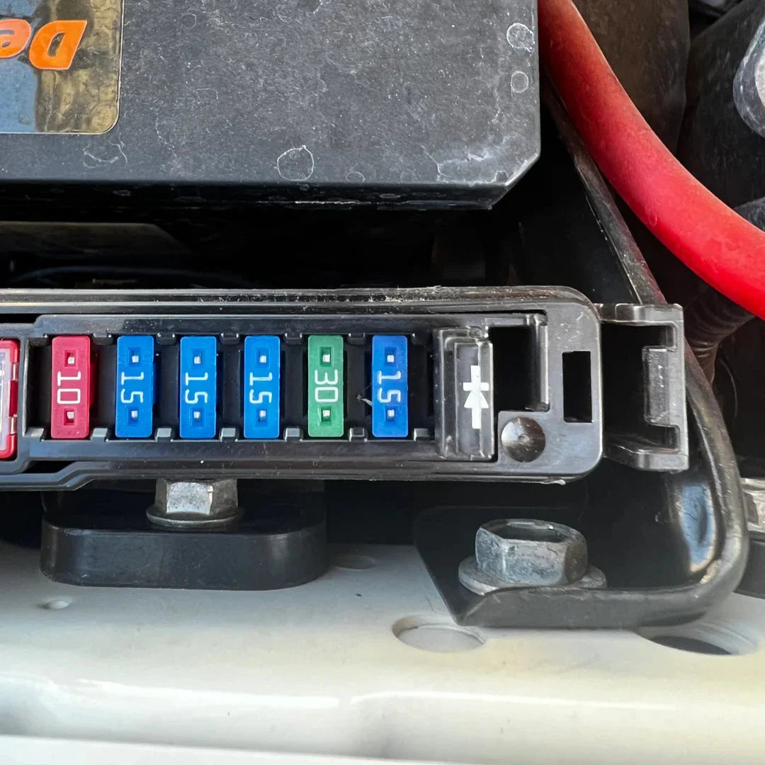 Car fuse box with colored fuses and visible branding on a vehicle interior.