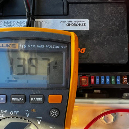 Multimeter displaying voltage reading with a car battery in the background