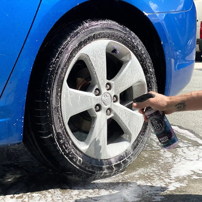 Person cleaning a car tire with a spray bottle on a blue car.