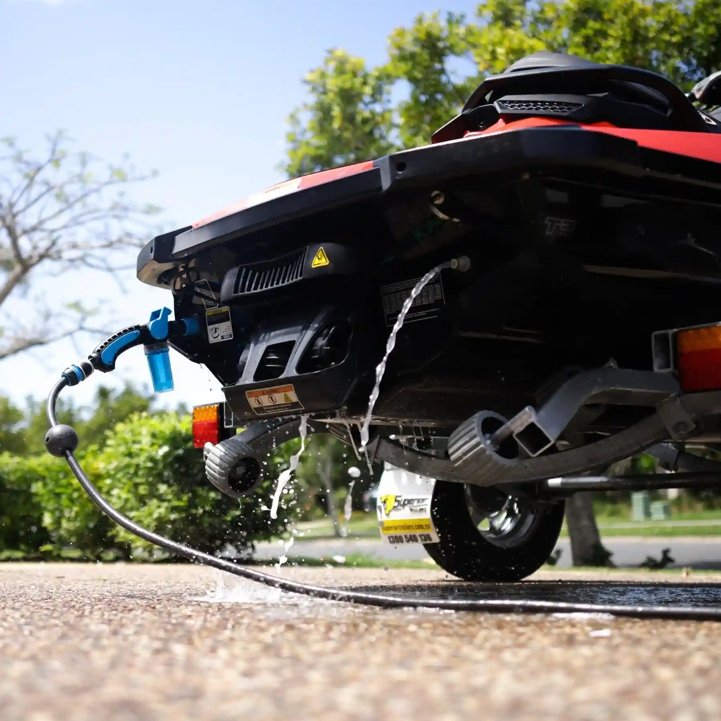 Back of a vehicle with a hose attached, spraying water outdoors.