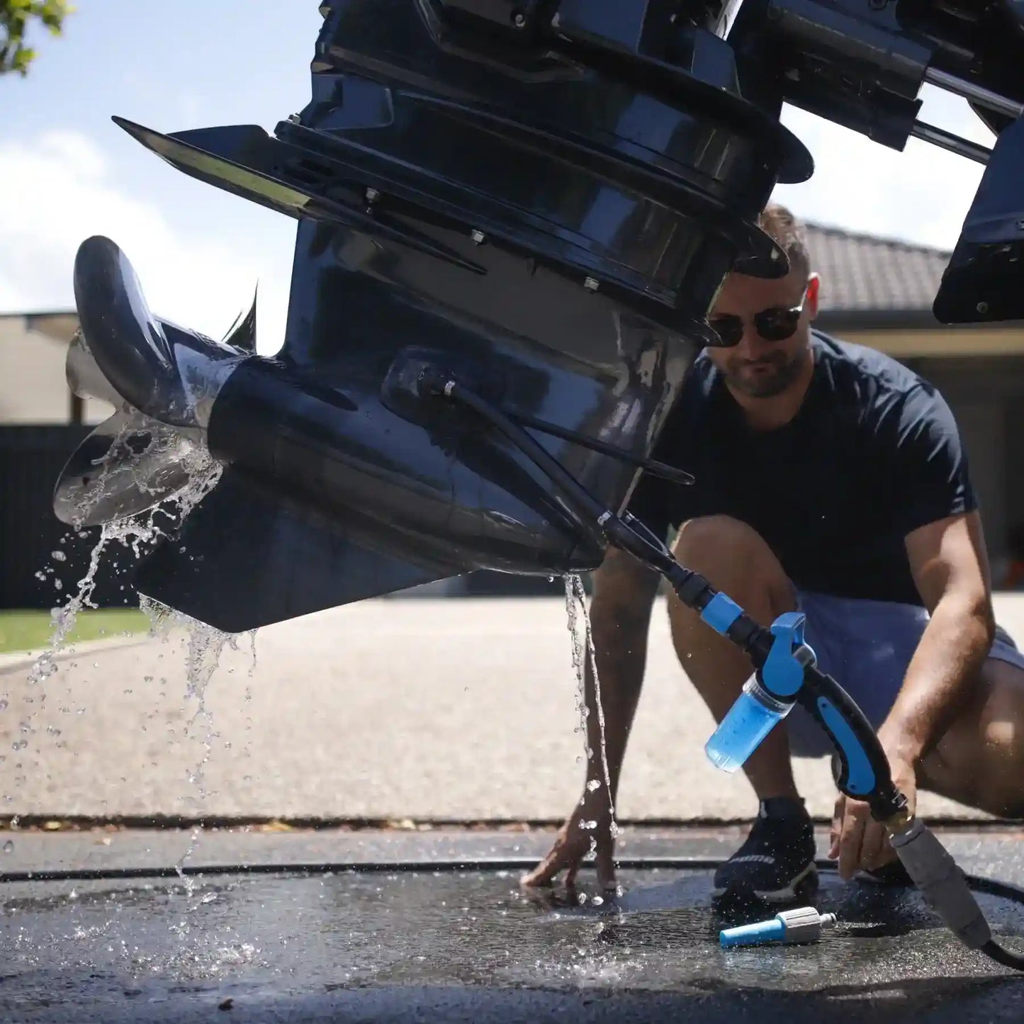 Person cleaning a boat propeller with a hose outdoors.