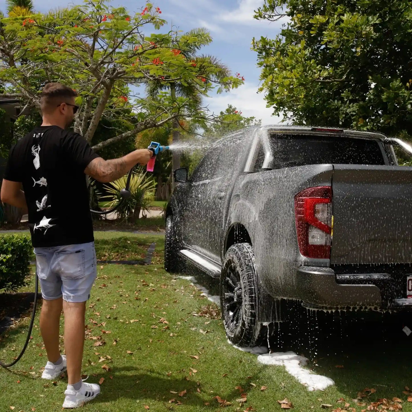 Person washing a black pickup truck with a garden hose outdoors.