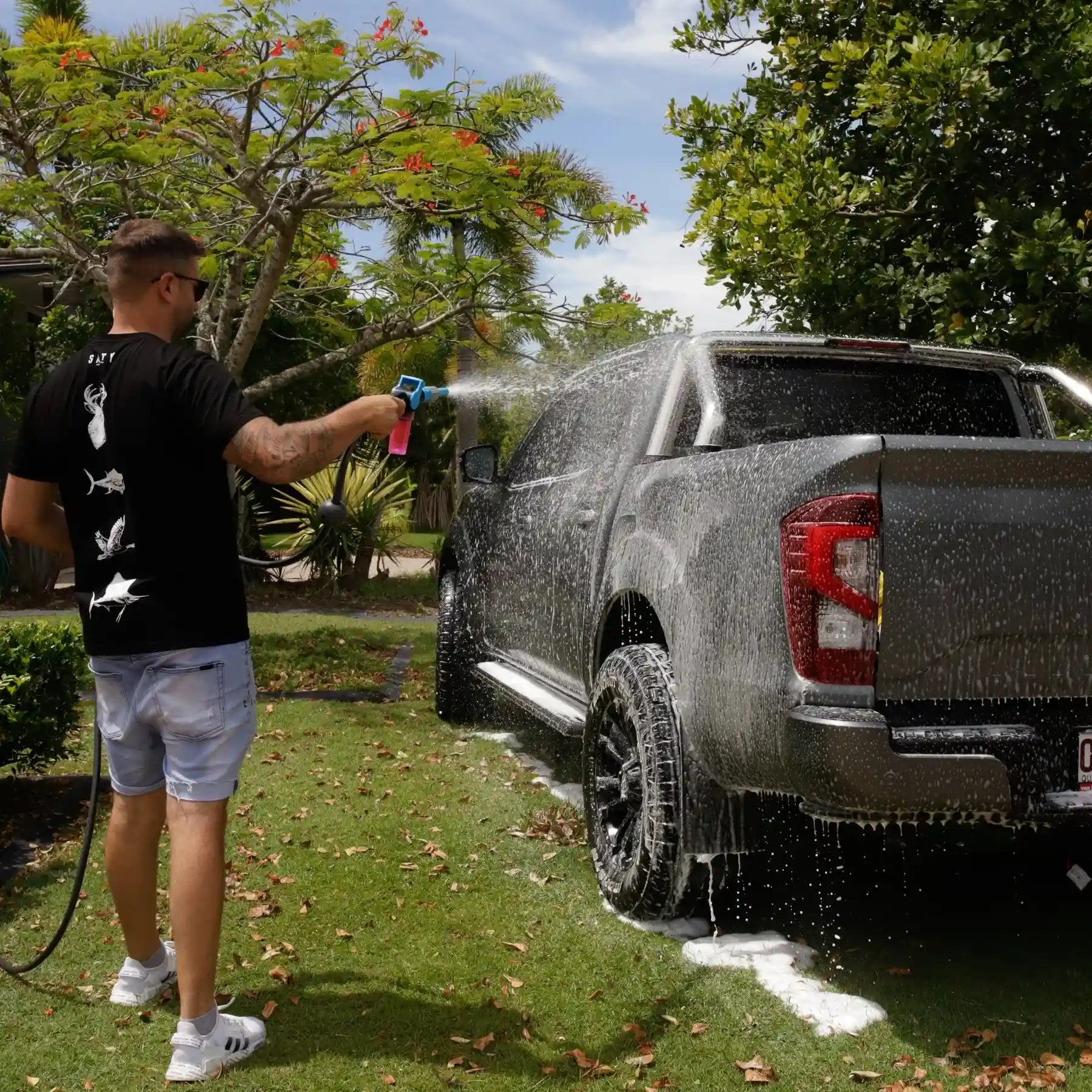 Person washing a black pickup truck with a garden hose outdoors.