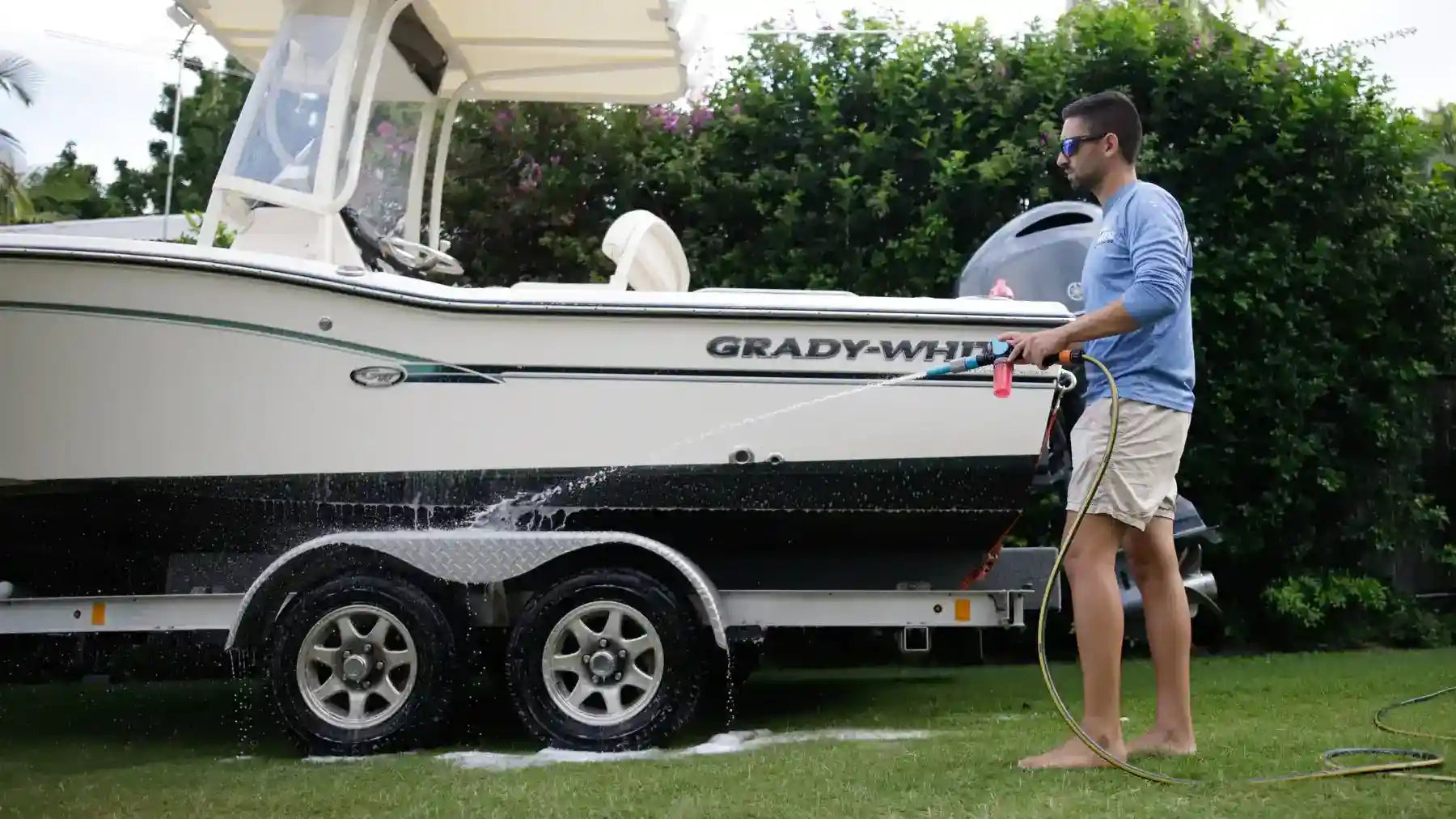 Man washing a Grady-White boat with a hose on a grassy area.