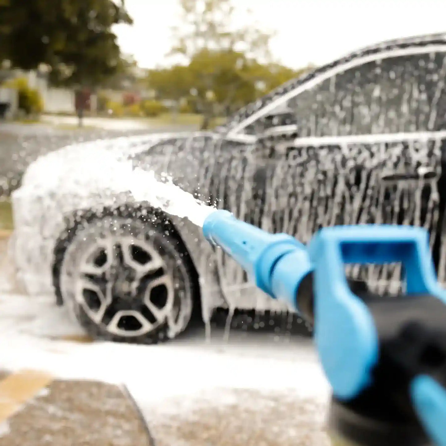 Car being washed with a blue spray gun in a driveway