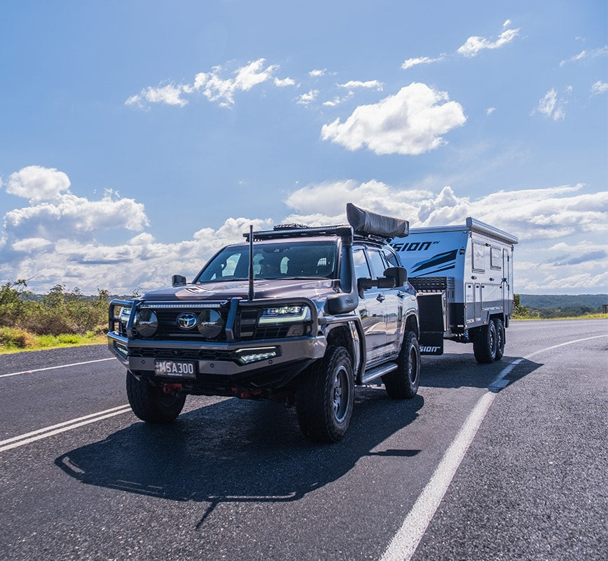 SUV towing a camper trailer on a road with a clear blue sky.