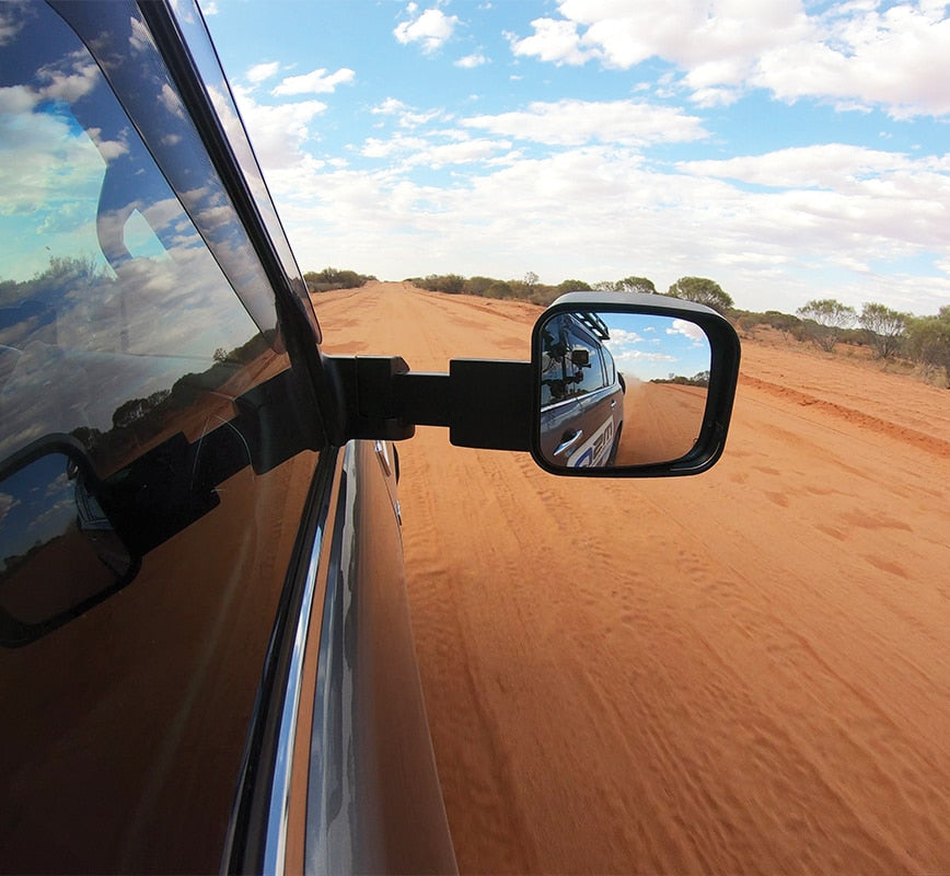 Side view mirror of a vehicle on a dirt road with a clear blue sky.