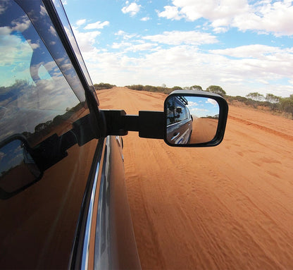 Side view mirror of a vehicle on a dirt road with a clear blue sky.