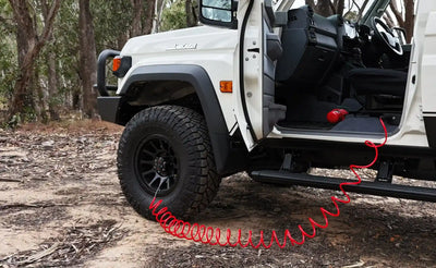 White off-road vehicle with a red tow air hose on a dirt path in a forest.