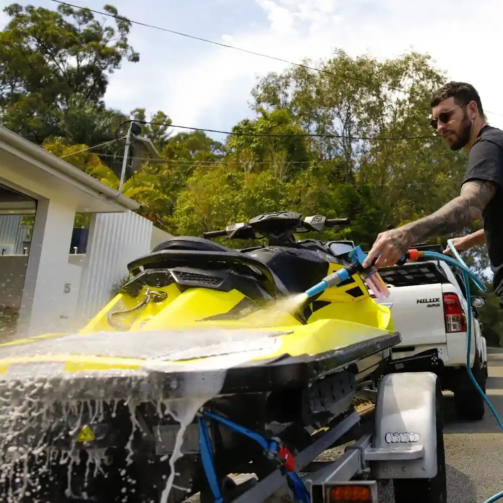 Person washing a yellow watercraft with a hose outdoors.
