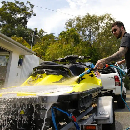 Person washing a yellow watercraft with a hose outdoors.
