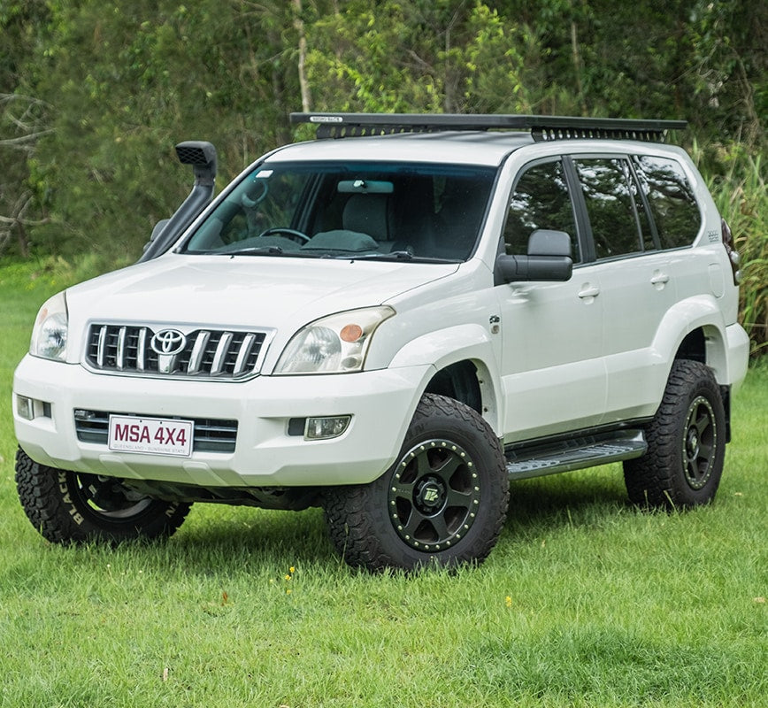 White Toyota SUV with off-road modifications on a grassy area with trees in the background