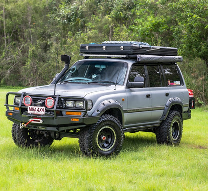 Silver off-road vehicle with roof racks in a grassy area with trees.