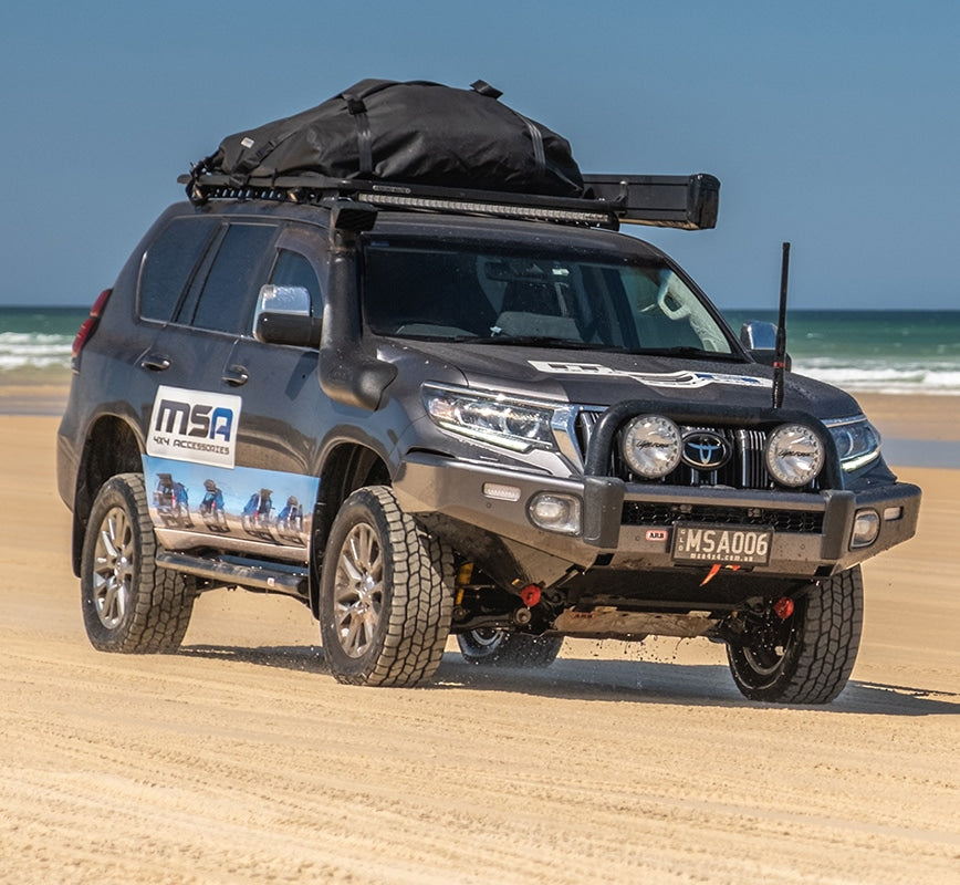 SUV with roof rack on a sandy beach with ocean in the background