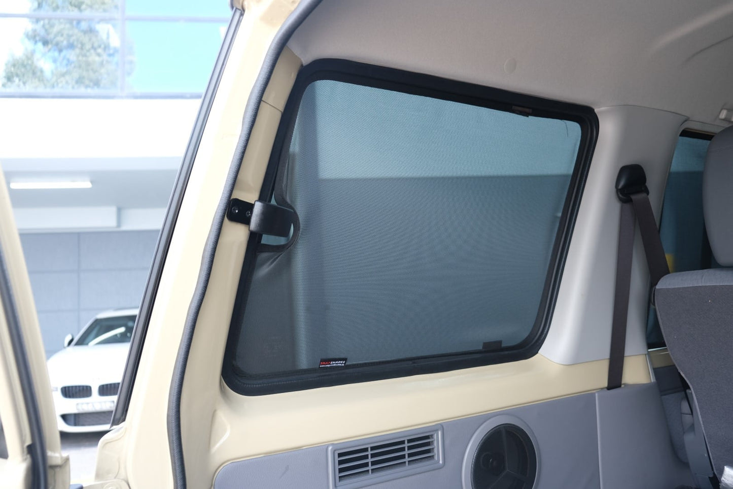 Car window with a sunshade inside a vehicle, with a blurred background of another car and building.