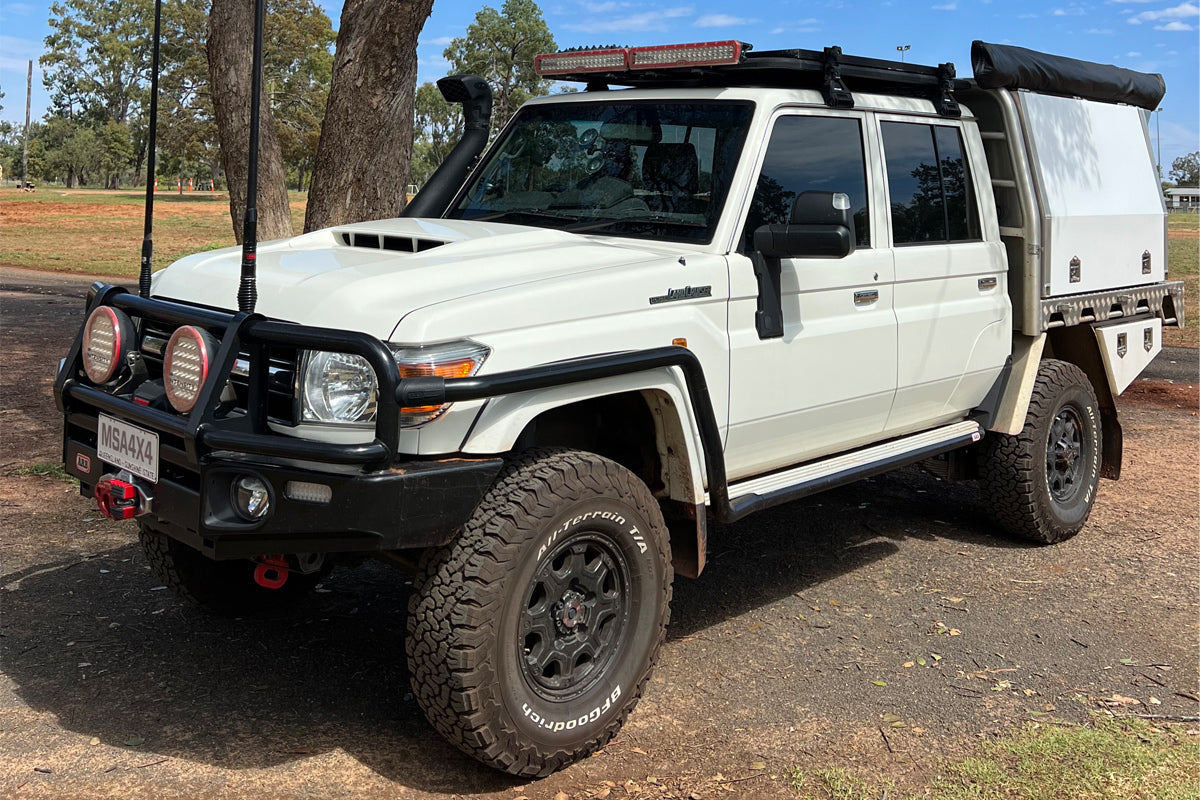 White off-road vehicle with roof rack and additional lights on a dirt road.